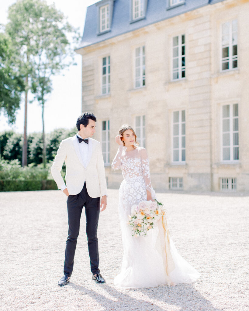 groom looking at bride adjusting her hair standing in front of french chateau wedding venue