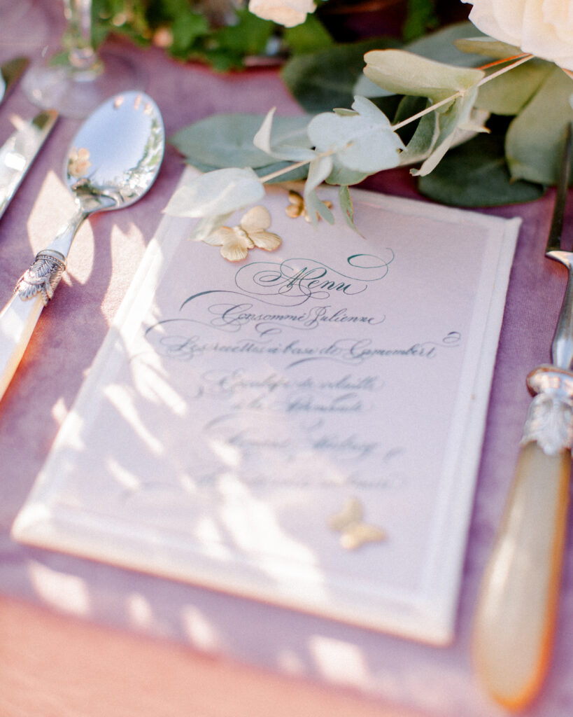 Calligraphy menu card with gold butterflies, purple velvet tablecloth at a french chateau wedding venue