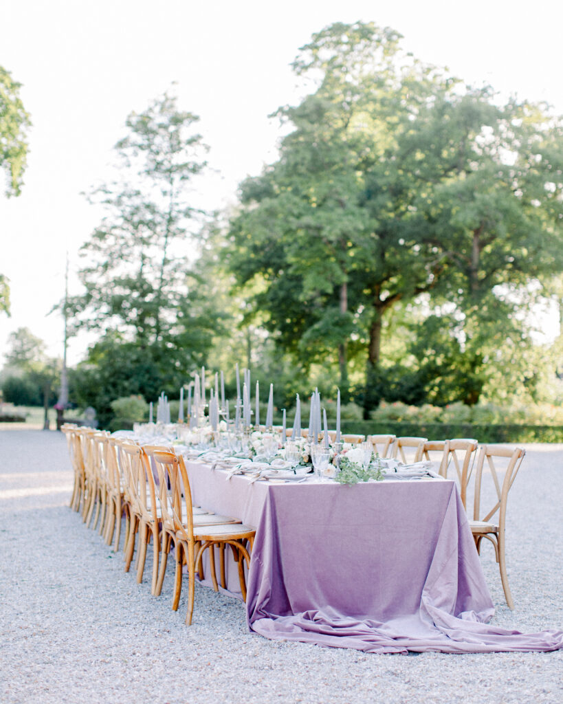 Head table set al fresco with bistro chairs, silver candelabras, purple velvet tablecloth, in the garden of a french chateau wedding venue.