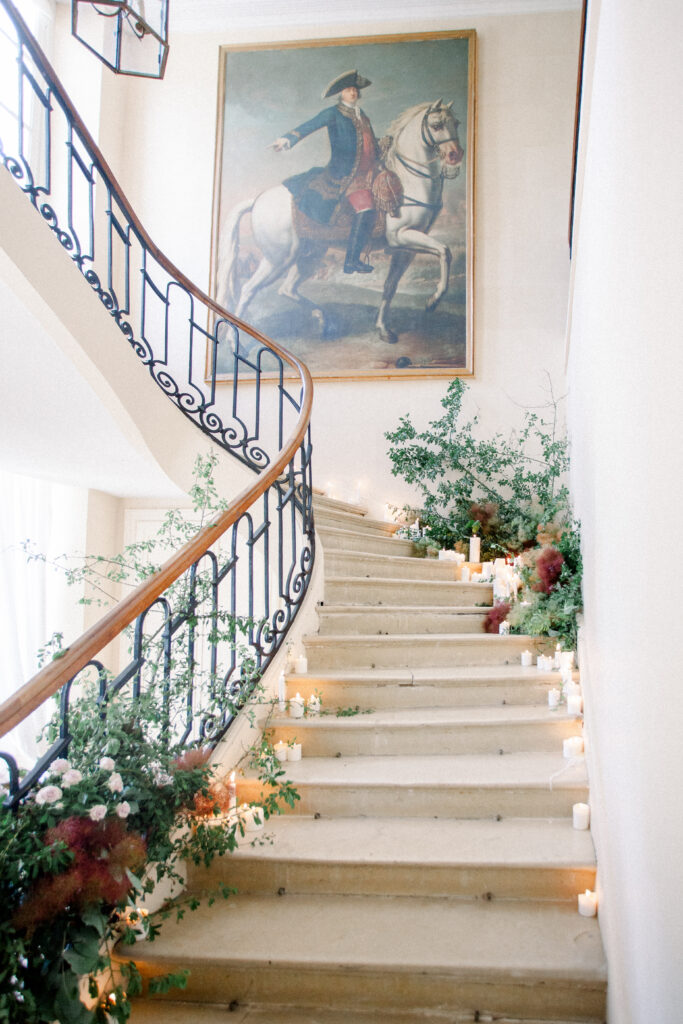 ornate staircase with stone steps, lush greenery, romantic candles, and heirloom painting in a french chateau wedding venue