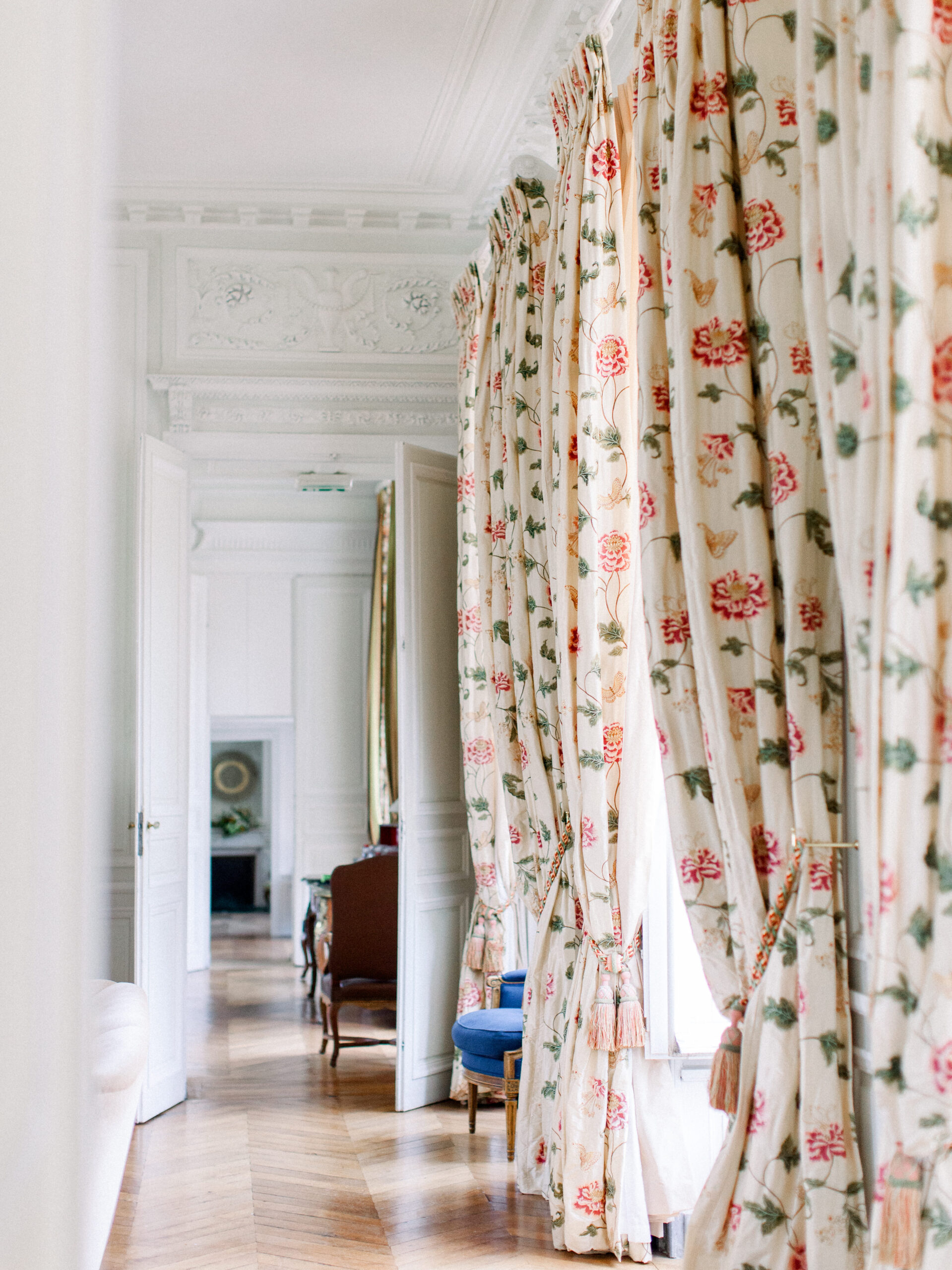 Ornate hallway with herringbone wood floors, floral drapery, and antique furniture inside a french chateau wedding venue.