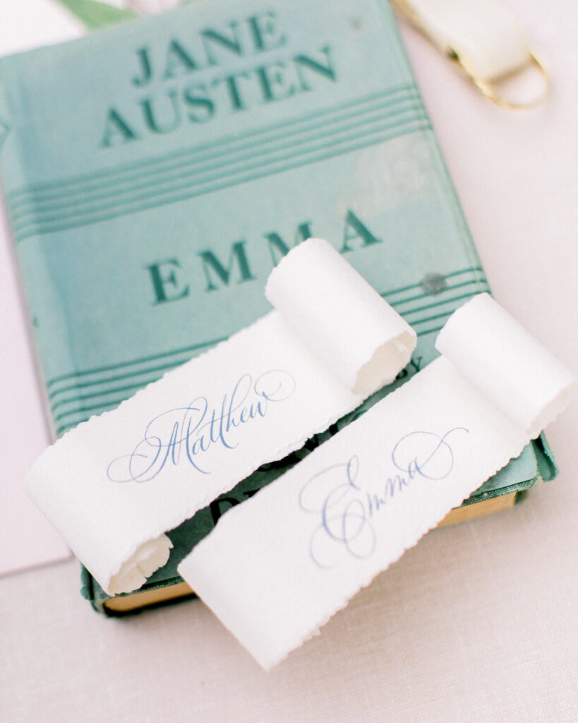 escort cards on deckled edge paper, sitting on top of the book Emma by Jane Austen, wedding day details
