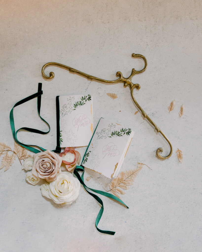 Wedding vow books with chamapgne and ivory florals and emerald green ribbon, with a vintage french market hanger, wedding day details by Boston wedding photographer Ashley Helen