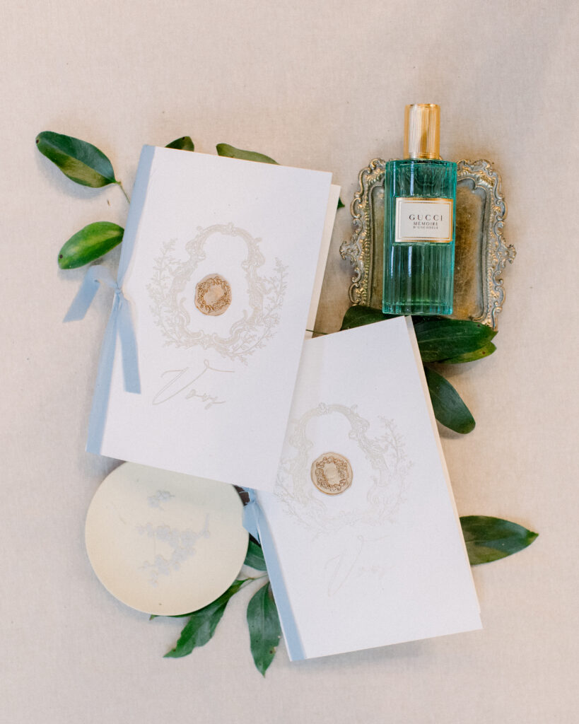 Elegant vow books with ornate crest and wax seal, and blue ribbon, with gucci perfume bottle, wedding day details by Boston wedding photographer Ashley Helen