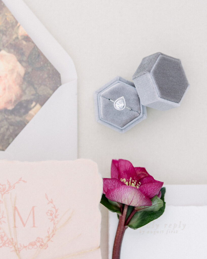 Pear shaped engagement ring in grey octagon velvet ring box, with blush wedding invitations and a deep pink flower, wedding day details by Boston wedding photographer Ashley Helen 