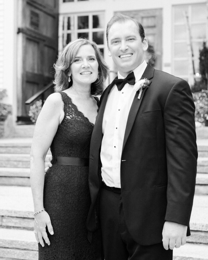 black and white photo of groom standing with his mother, arm around her waist