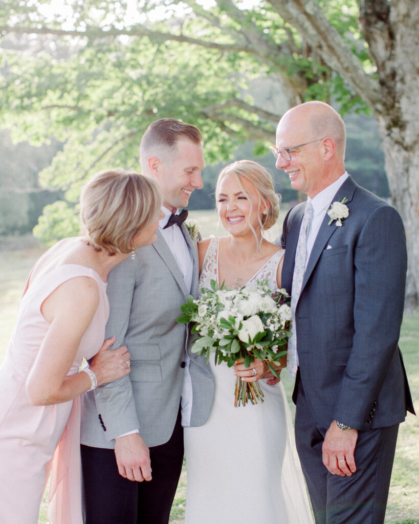 wedding couple with their parents, turned and laughing together, wedding family photos